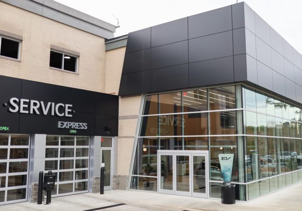 Modern glass-front exterior of Julio Jones Kia dealership with electric vehicle charging stations and parking spaces in the foreground.