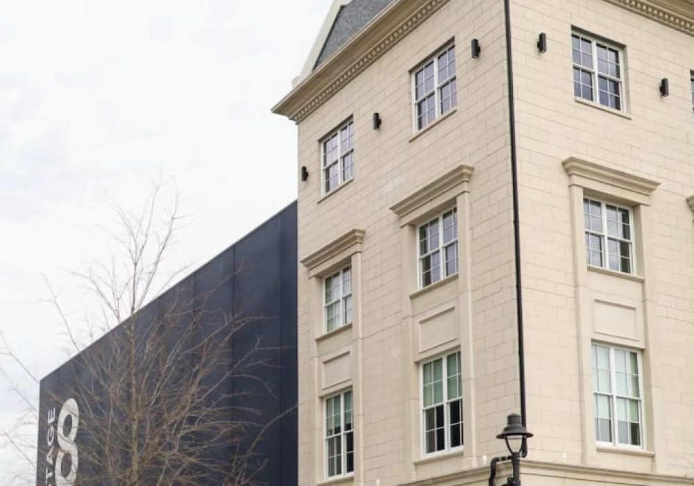 A grand, cream-colored townhouse next to a large "Stage 8" film studio, highlighting a mix of elegance and industry.