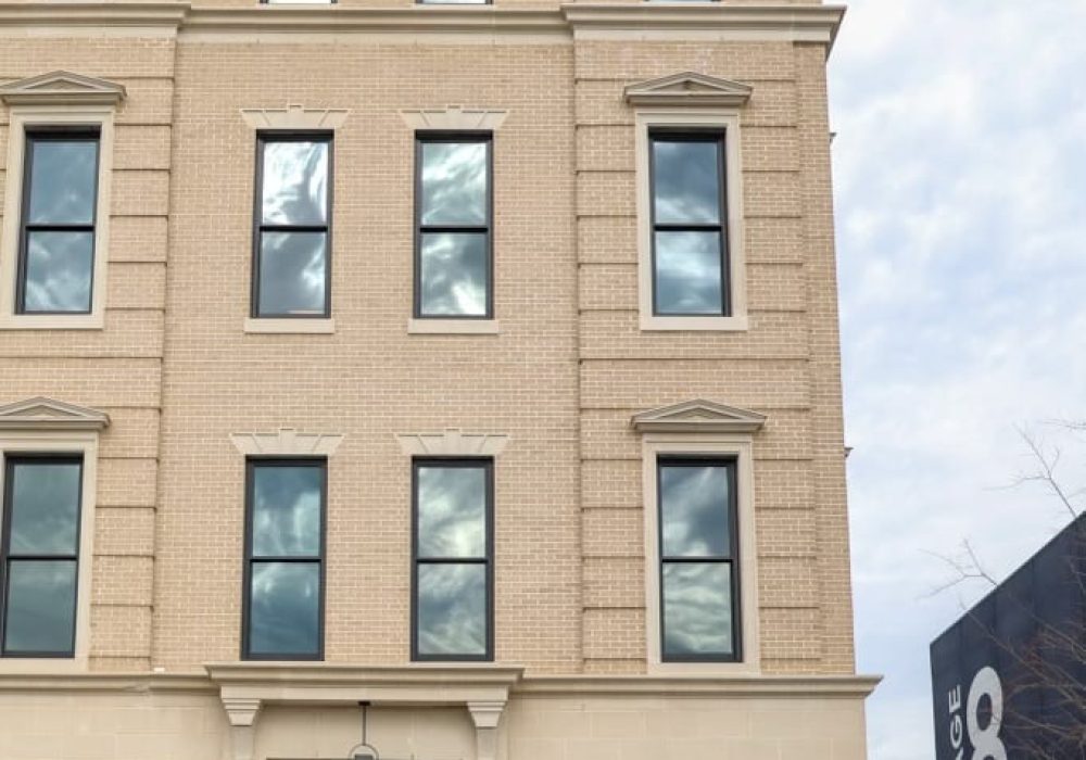 A grand, four-story townhouse with an elegant beige brick exterior and black-trimmed windows.