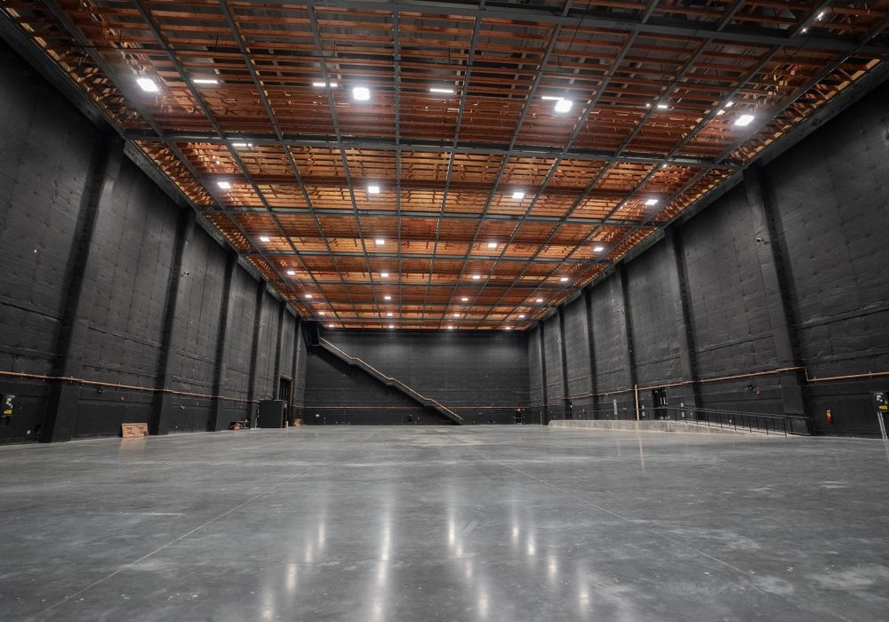 A spacious soundstage with black walls, polished concrete floors, and advanced lighting setup, ideal for film production.