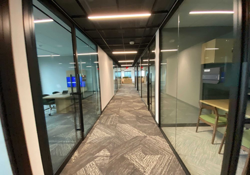 A hallway with glass-walled conference rooms, featuring sleek black frames and contemporary office decor.