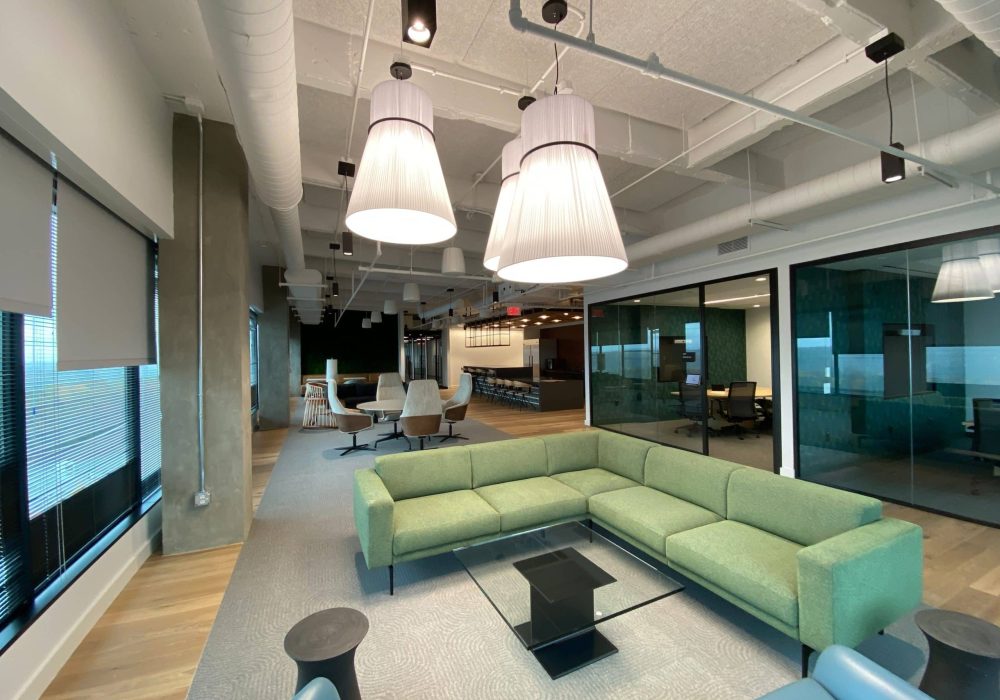 Open-concept office lounge with green sectional seating and contemporary pendant lighting.