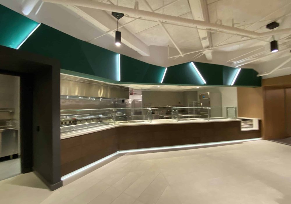 Modern cafeteria space with a sleek service counter and industrial ceiling lighting.