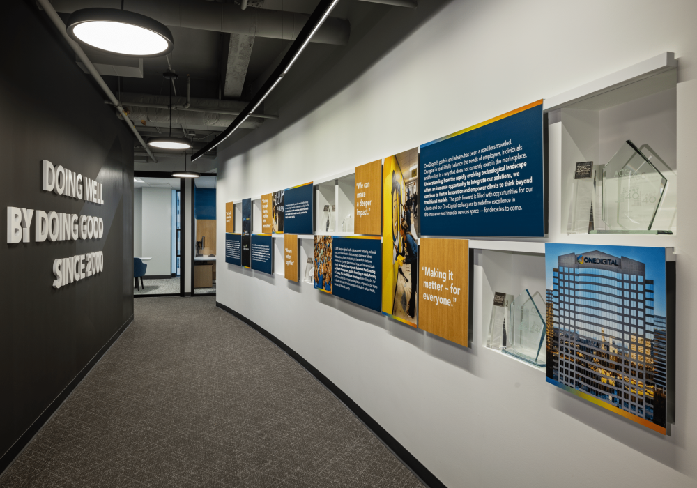 A curved hallway display featuring OneDigital’s history, mission, and awards, with motivational quotes and company milestones.