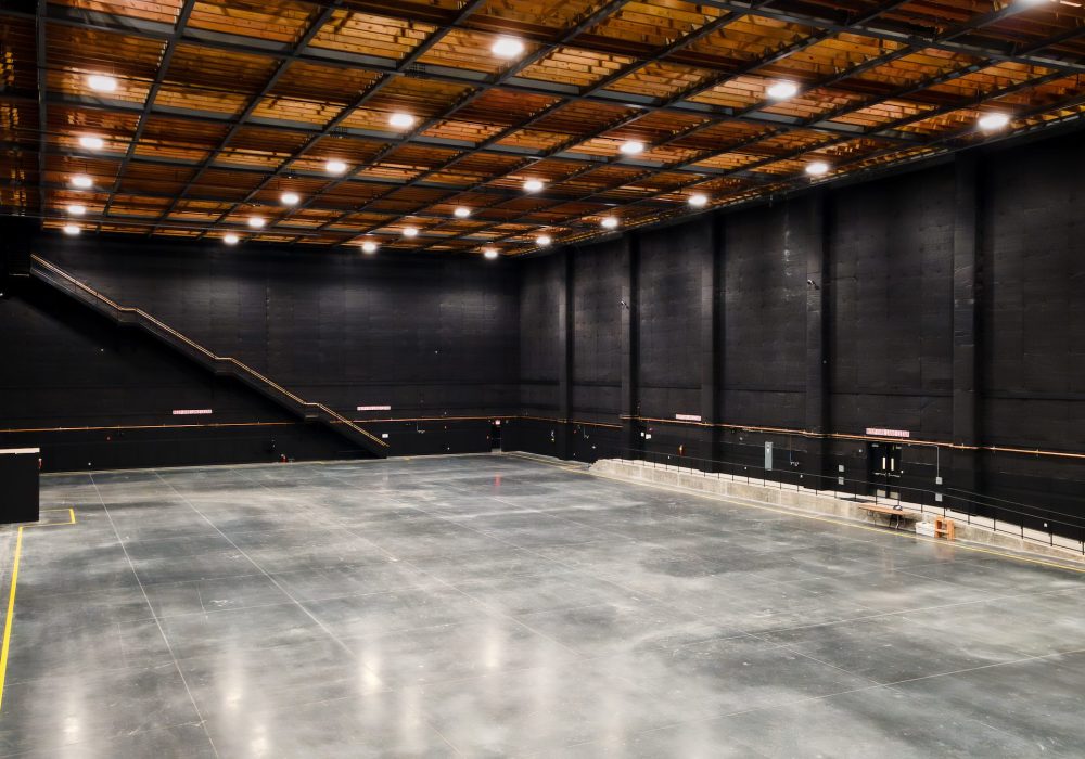 A large soundstage interior with black acoustic walls, high ceilings, and wooden support beams designed for film production.